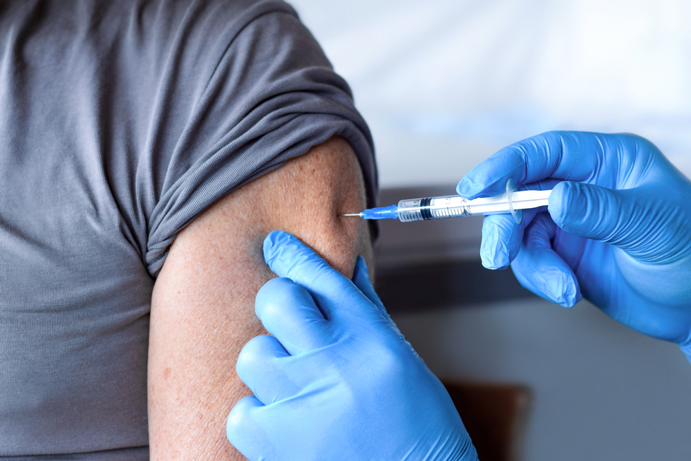 Elderly man getting COVID booster by a pharmacist with gloves on