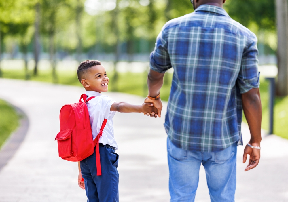 schoolboy on the way to school with backpack holding hand of father, while going to first grade on sunny autumn day through park