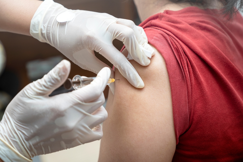 A woman is getting a shot in her arm. The nurse is wearing gloves and holding a syringe
